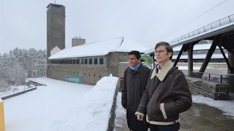 Zwei Männer stehen neben einem der historischen Gebäude im verschneiten Vogelsang.