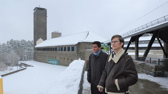 Zwei Männer stehen neben einem der historischen Gebäude im verschneiten Vogelsang.