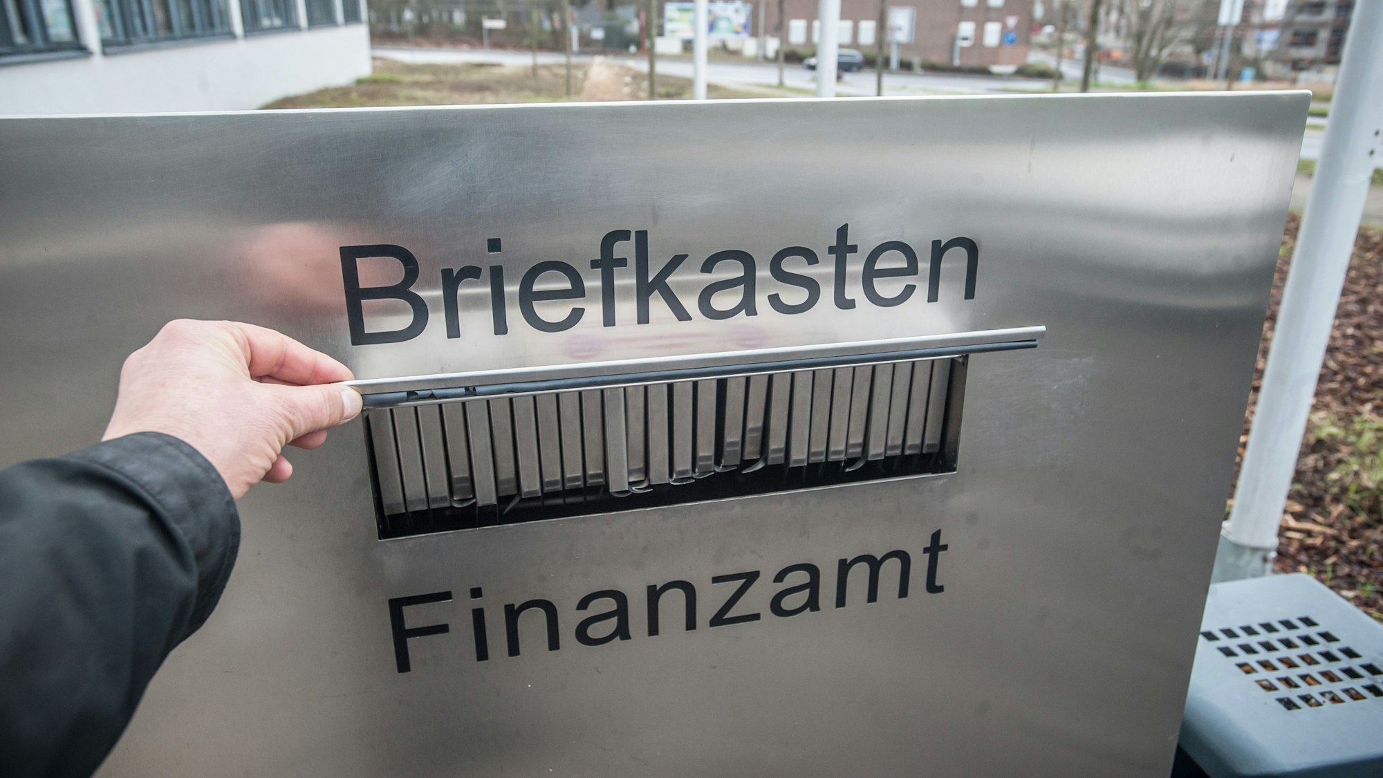 Eine Hand hält die Klappe am Briefkasten des Leverkusener Finanzamts auf.