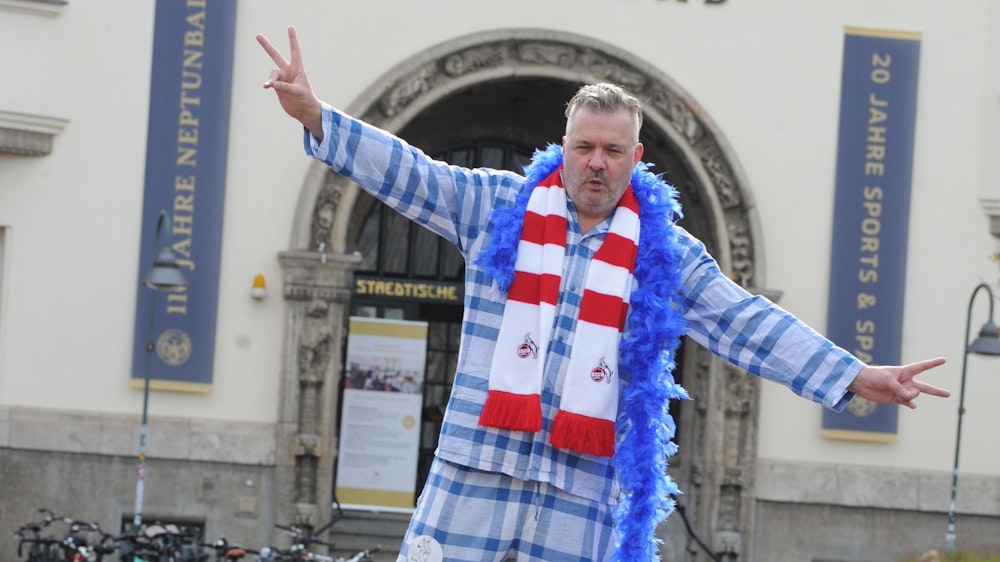 Martin Bechler von der Kölner Band Fortuna Ehrenfeld steht im charakteristischen Schlafanzug und mit einem Schal des 1. FC Köln vor dem Ehrenfelder Neptunbad.