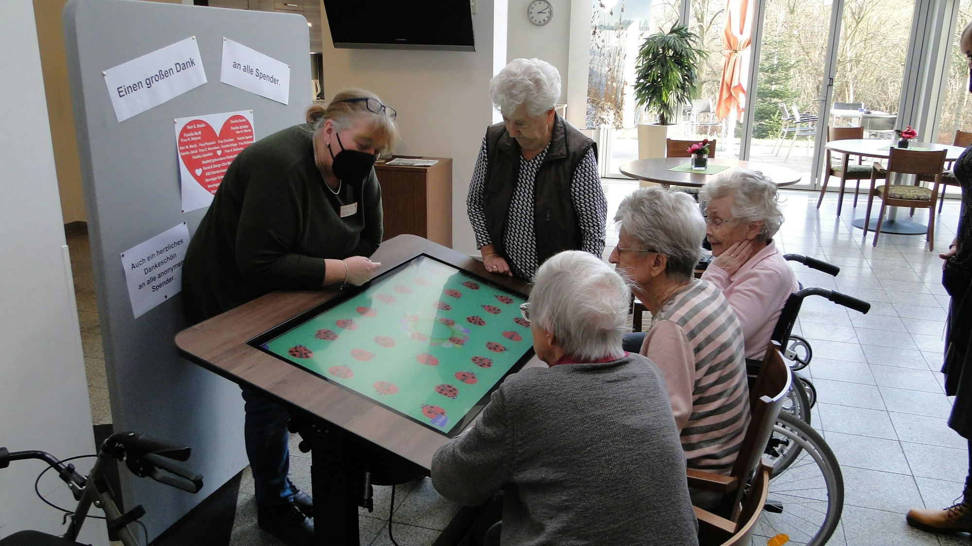 Der neue digitale Spieletisch mit vier älteren Frauen und einer Pflegerin, die etwas erklärt.