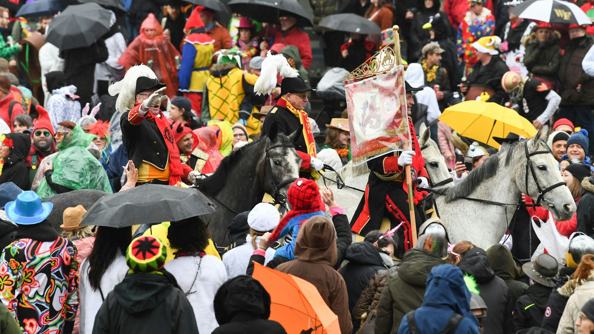 Eine Gruppe zu Pferd reitet beim Rosenmontagszug durch die Menge.