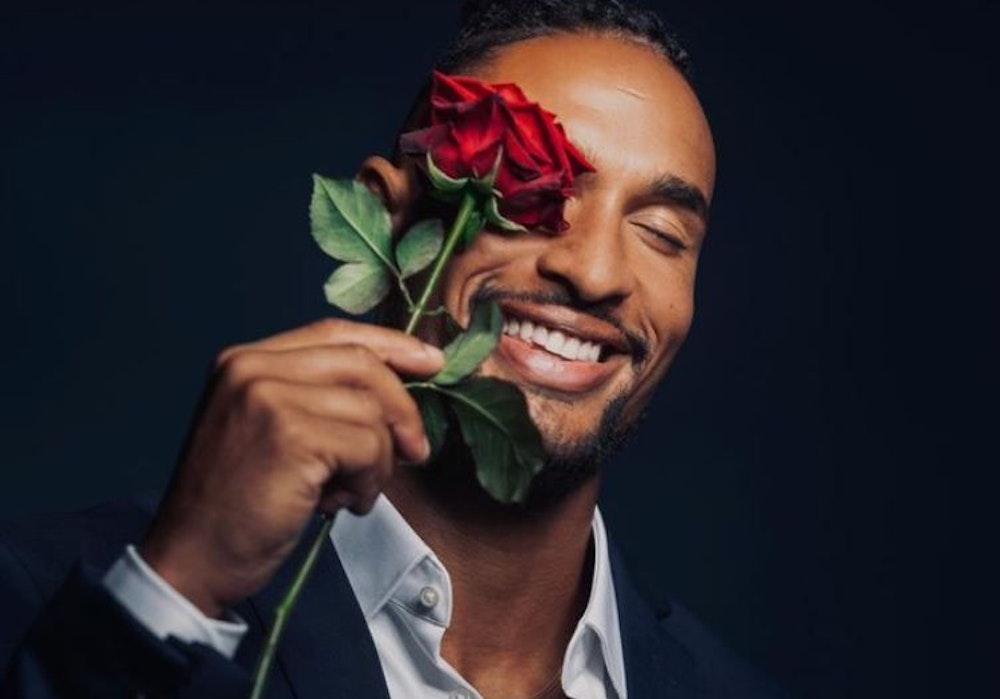 Er ist der neue „Bachelor“: David Jackson geht auf Liebessuche im TV. Er hält sich eine Rose vor sein Auge und trägt ein Anzug.