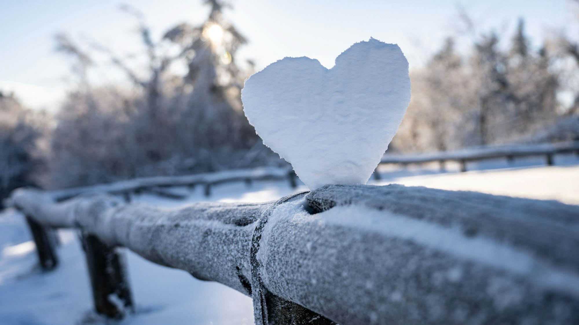 Ein weißes Herz aus Schnee auf einem Holzzaun.