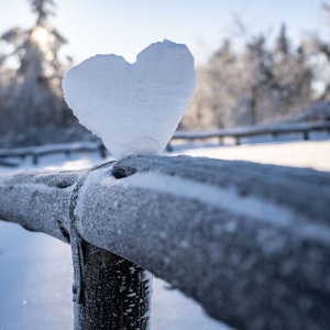 Ein weißes Herz aus Schnee auf einem Holzzaun.