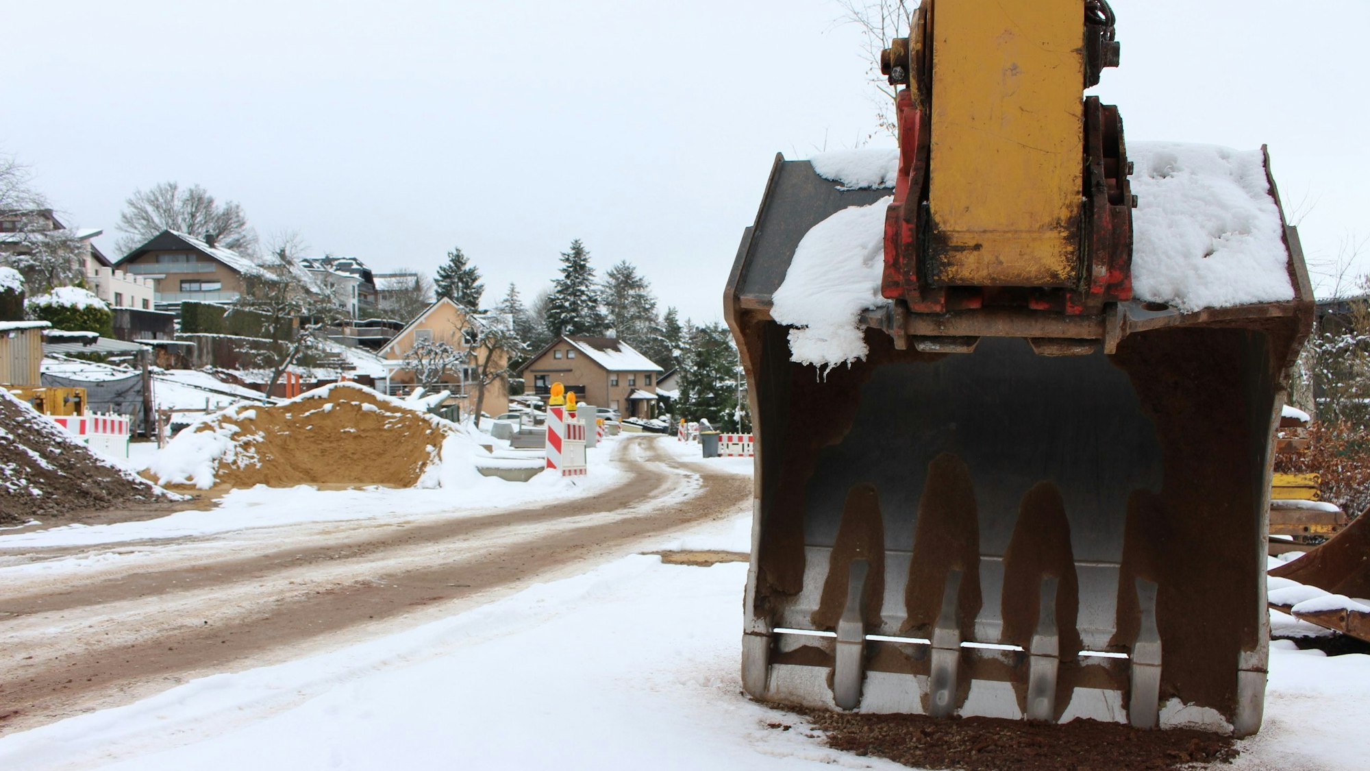 Eine Baggerschaufel steht an einer Straßenbaustelle, auf der wegen des Schnees nicht gearbeitet wird.