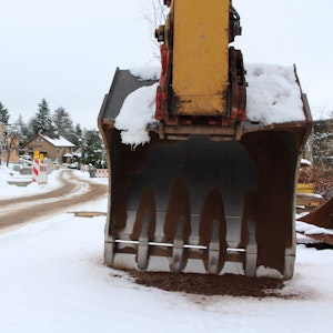 Eine Baggerschaufel steht an einer Straßenbaustelle, auf der wegen des Schnees nicht gearbeitet wird.