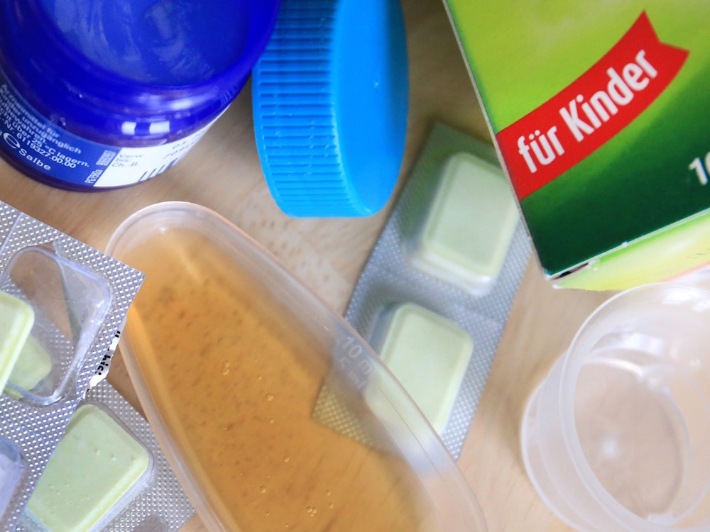 Medikamente wie Hustensaft, Lutschtabletten und Salbe stehen auf einem Tisch in einer Wohnung.