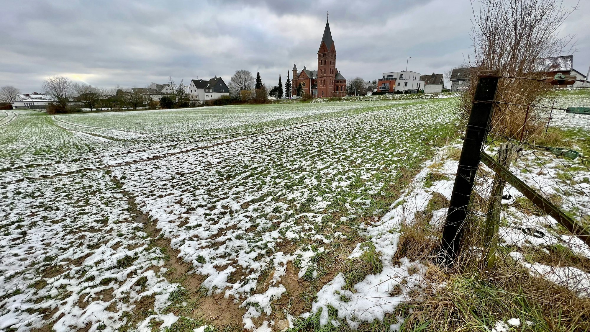Feld mit etwas Schnee, im Hintergrund die Kirche von Neuboddenberg und Häuser