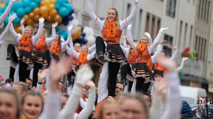Orange gekleidete Karnevlistinnen und Karnevalisten ziehen beim Rosenmontagszug 2020 durch die Kölner Straßen.