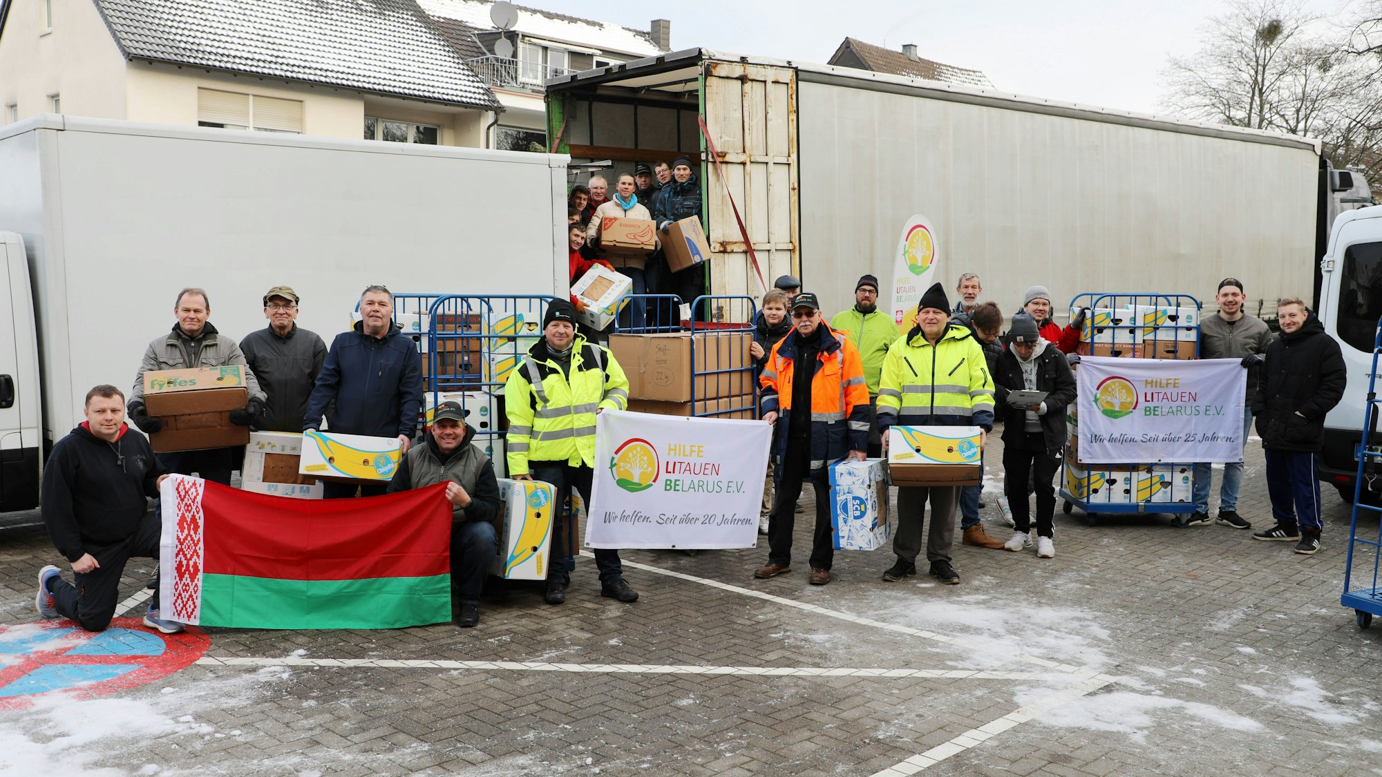 Helfer stehen mit der Fahne von Belarus und des Vereins Hilfe Litauen Belarus vor einem Lkw, der beladen wird.