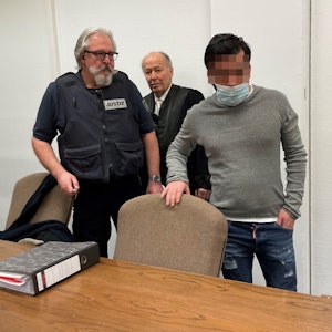 Das Bild zeigt den den Angeklagten mit einem Wachtmeister und seinem Verteidiger beim Prozess im Kölner Amtsgericht.