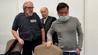 Das Bild zeigt den den Angeklagten mit einem Wachtmeister und seinem Verteidiger beim Prozess im Kölner Amtsgericht.