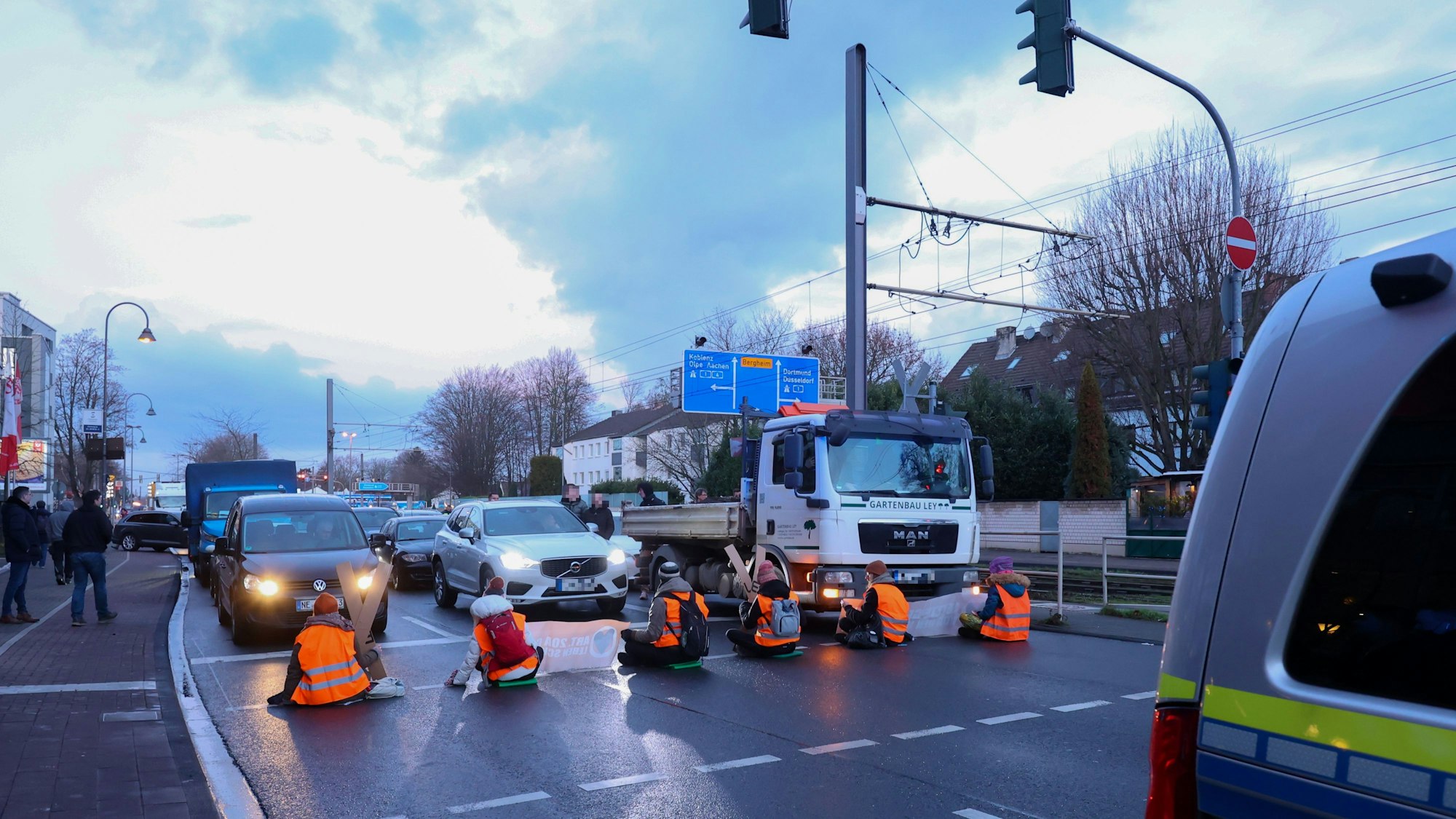 Männer und Frauen sitzen auf der Straße und blockieren für eine Klima-Demo den Verkehr.