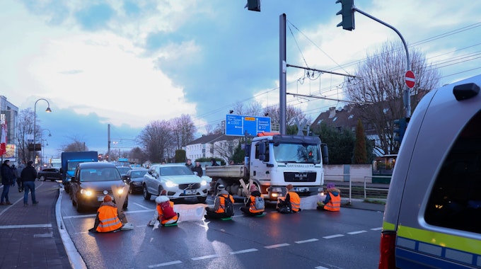 Männer und Frauen sitzen auf der Straße und blockieren für eine Klima-Demo den Verkehr.