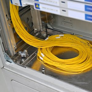 Ein Bündel gelber Glasfaserkabel liegt in einem Verteilerkasten.