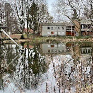 Das Alkenrather Gemeindezentrum, an dessen Stelle eine Kita und ein Seniorenwohnhaus entstehen sollen, im Vordergrund der Teich im Park