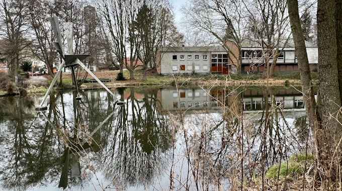 Das Alkenrather Gemeindezentrum, an dessen Stelle eine Kita und ein Seniorenwohnhaus entstehen sollen, im Vordergrund der Teich im Park