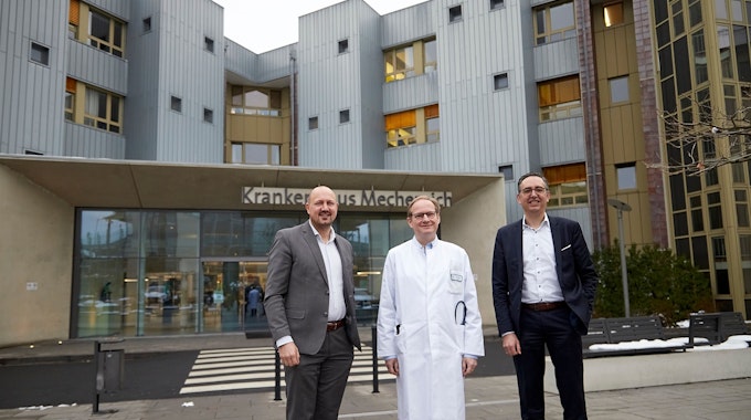 Drei Männer, der Mittlere im Arztkittel, stehen vor dem Eingang zum Kreiskrankenhaus Mechernich.