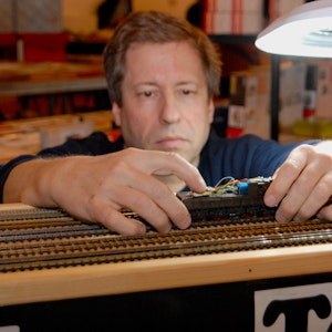 Bahndoktor Dirk Gardemann in seiner Fachwerkstatt mit einer Spielzeugeisenbahn in der Hand.