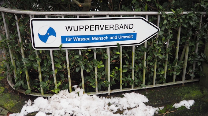 Ein Wegweiser mit der Aufschrift „Wupperverband für Wasser, Mensche und Umwelt“ vor einer grünen Hecke an einem Zaun vor der Verbandszentrale in Wuppertal.