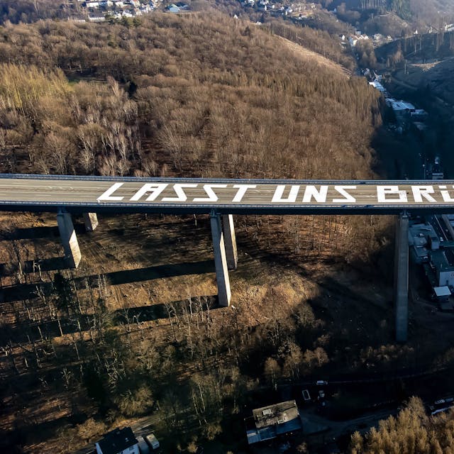 Lüdenscheid: Die Luftaufnahme zeigt die riesige Friedensbotschaft: „Lasst uns Brücken bauen“ auf der gesperrten Rahmedetal-Brücke der Autobahn 45 bei Lüdenscheid (Nordrhein-Westfalen).