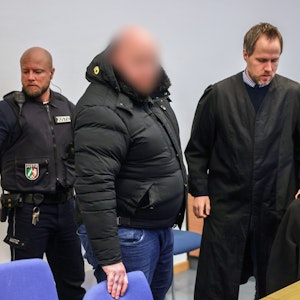 Der Angeklagte (M) steht im Gerichtssaal neben seinem Verteidiger Ingmar Rosentreter (r). Der Mann steh wegen Beteiligung an den Krawallen beim Conference-League-Spiel des 1. FC Köln in Nizza vor Gericht.