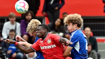 Ein Fußballer setzt sich gegen zwei Gegenspieler im Kopfball durch.