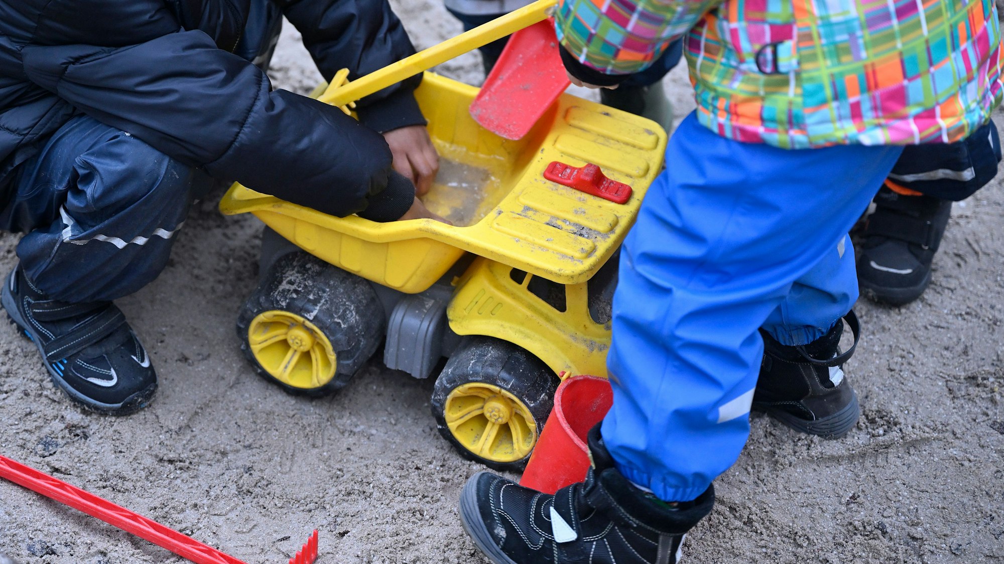 Kinder spielen mit einem gelben Spielzeugbagger im Sand.