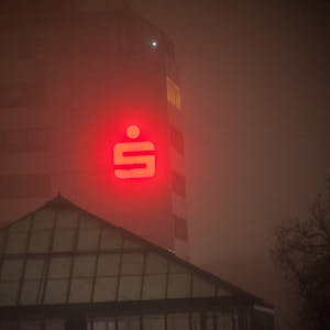 Das rote Logo der Sparkasse Leverkusen an der Fassade des Sparkassen-Gebäudes in Leverkusen-Wiesdorf durchdringt den Nebel.