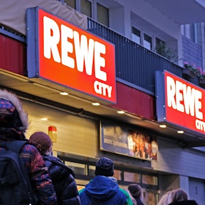 Kundinnen und Kunden vor einem REWE-Supermarkt.