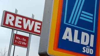 Schilder des Discounters Aldi Süd und der Supermarktkette Rewe stehen an der Zufahrt eines Industriegebiets in Glashütten (Hessen).