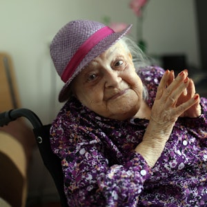 Faye Cukier trägt an ihrem 100. Geburtstag ein lila Hütchen und ein lila Hemd. Sie schaut lächelnd in die Kamera.