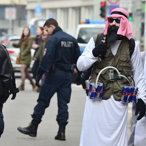 Ein als Terrorist verkleideter Karnevalist mit „Sprengstoffgürtel“ aus Energy-Drinks steht während der Karnevalszeit am 15. Februar 2015 neben Polizisten.