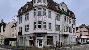 Ein vierstöckige Altbau an einer Straßenecke mit weißer Fassade ist zu sehen.