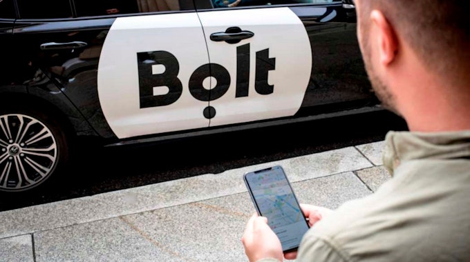 Ein Mann mit Smartphone steht vor einem Bolt-Auto