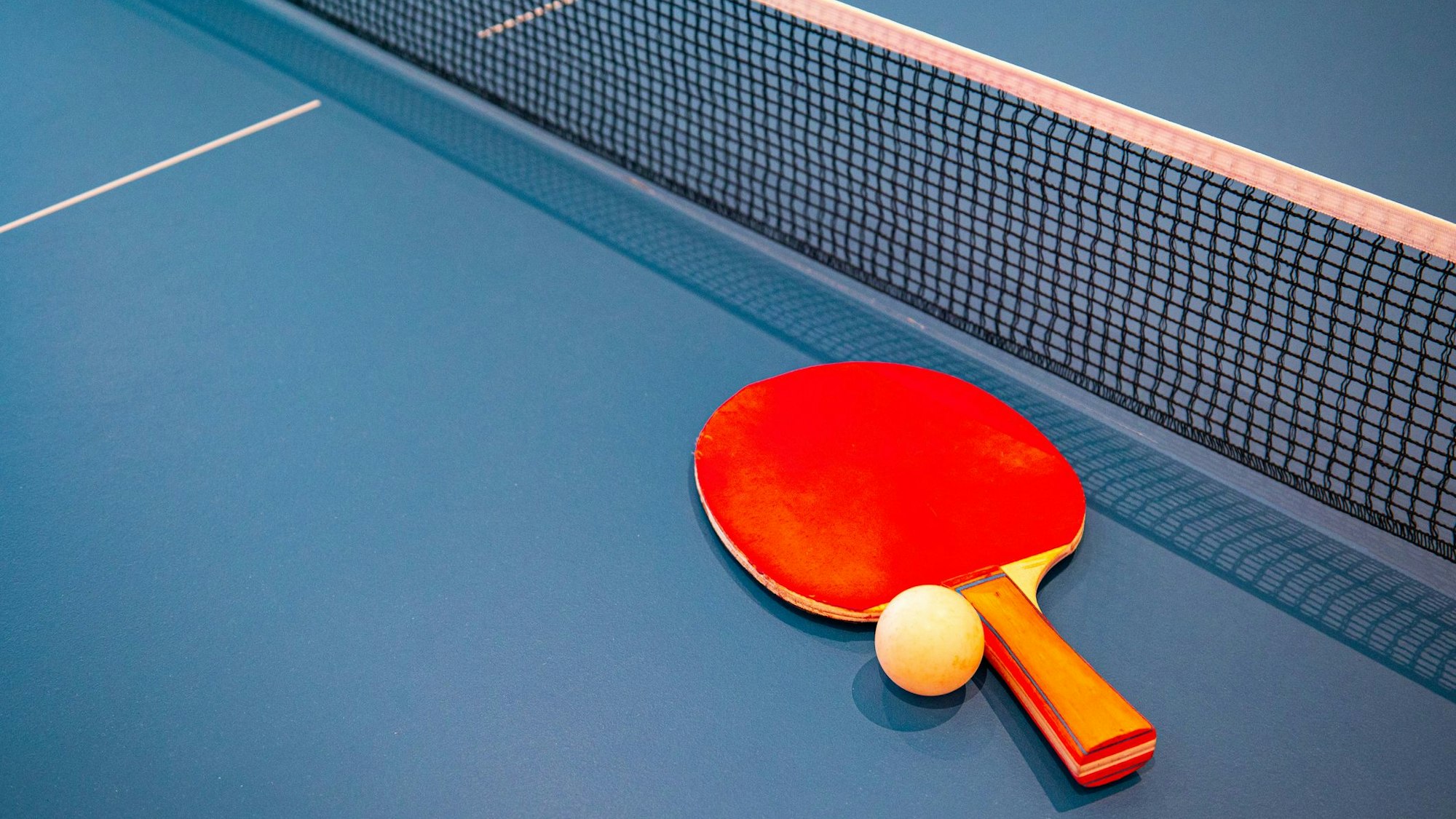Ein Tischtennisschläger samt Ball liegen auf einer blauen Platte.