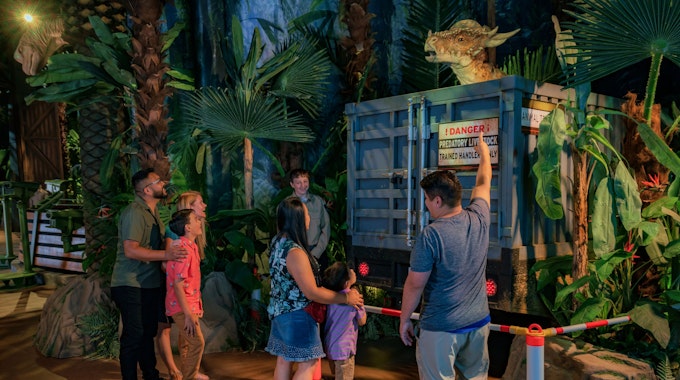 Mehrere Besucher der Jurassic-World-Ausstellung stehen vor einem Modell-Dinosuarier.