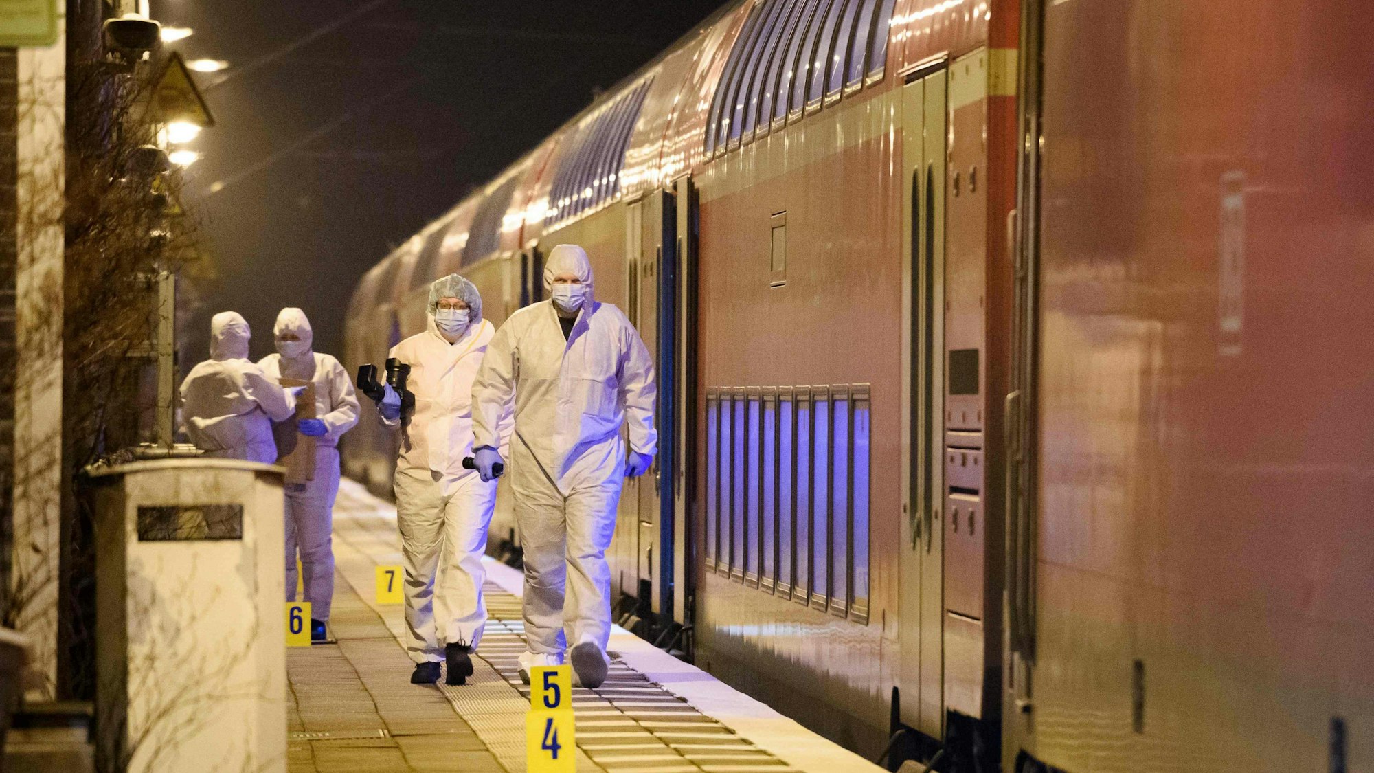 Forensiker der Polizei laufen in weißen Schutzanzügen und mit Masken über den Bahnsteig in Brolstedt. Neben ihnen steht der Regionalzug, in dem ein 33 Jahre alter Mann mutmaßlich zwei Menschen getötet und sieben verletzt hat.