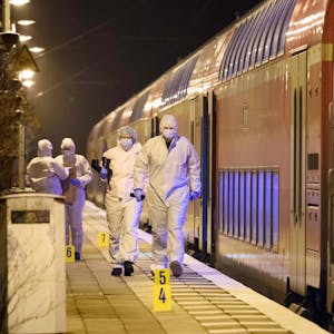 Forensiker der Polizei laufen in weißen Schutzanzügen und mit Masken über den Bahnsteig in Brolstedt. Neben ihnen steht der Regionalzug, in dem ein 33 Jahre alter Mann mutmaßlich zwei Menschen getötet und sieben verletzt hat.