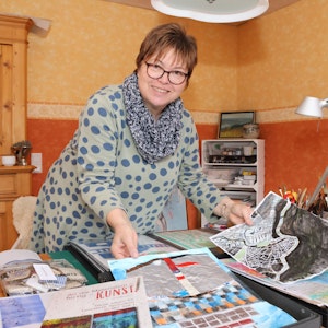 Die Autorin Silvia Hillringhaus an einem Tisch mit Malereien.