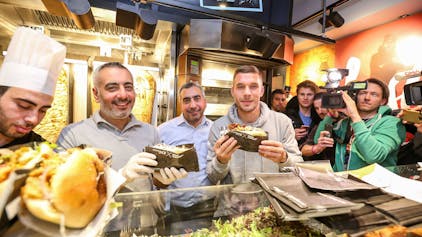 Lukas Podolski posiert mit Kollegen bei der Eröffnung eines Mangal-Döner-Ladens. Die Presse und Fans stehen im Hintergrund.