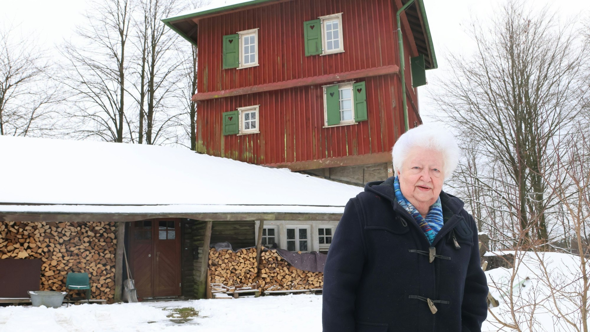 Eine Frau steht vor dem verschneiten Blockhaus aus Holz.