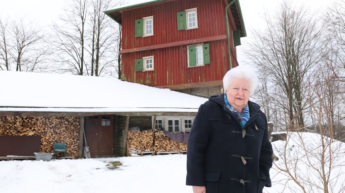 Eine Frau steht vor dem verschneiten Blockhaus aus Holz.