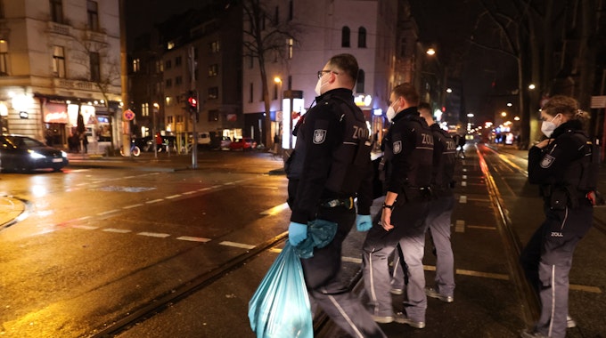 Einsatzkräfte des Zolls gehen mit sichergestelltem Material über eine Straße in Köln.