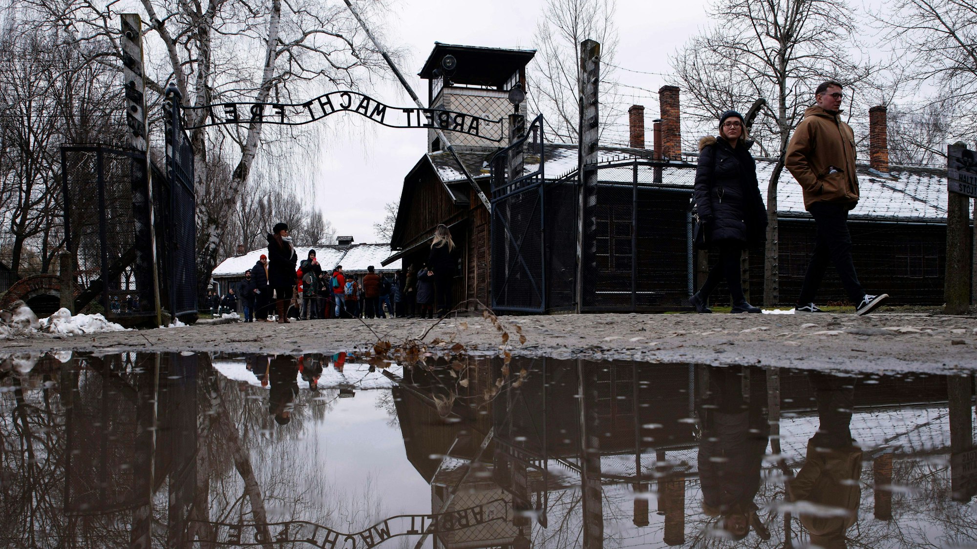 Menschen gehen neben dem „Arbeit Macht Frei“-Tor des ehemaligen deutschen Konzentrations- und Vernichtungslagers Auschwitz-Birkenau.
