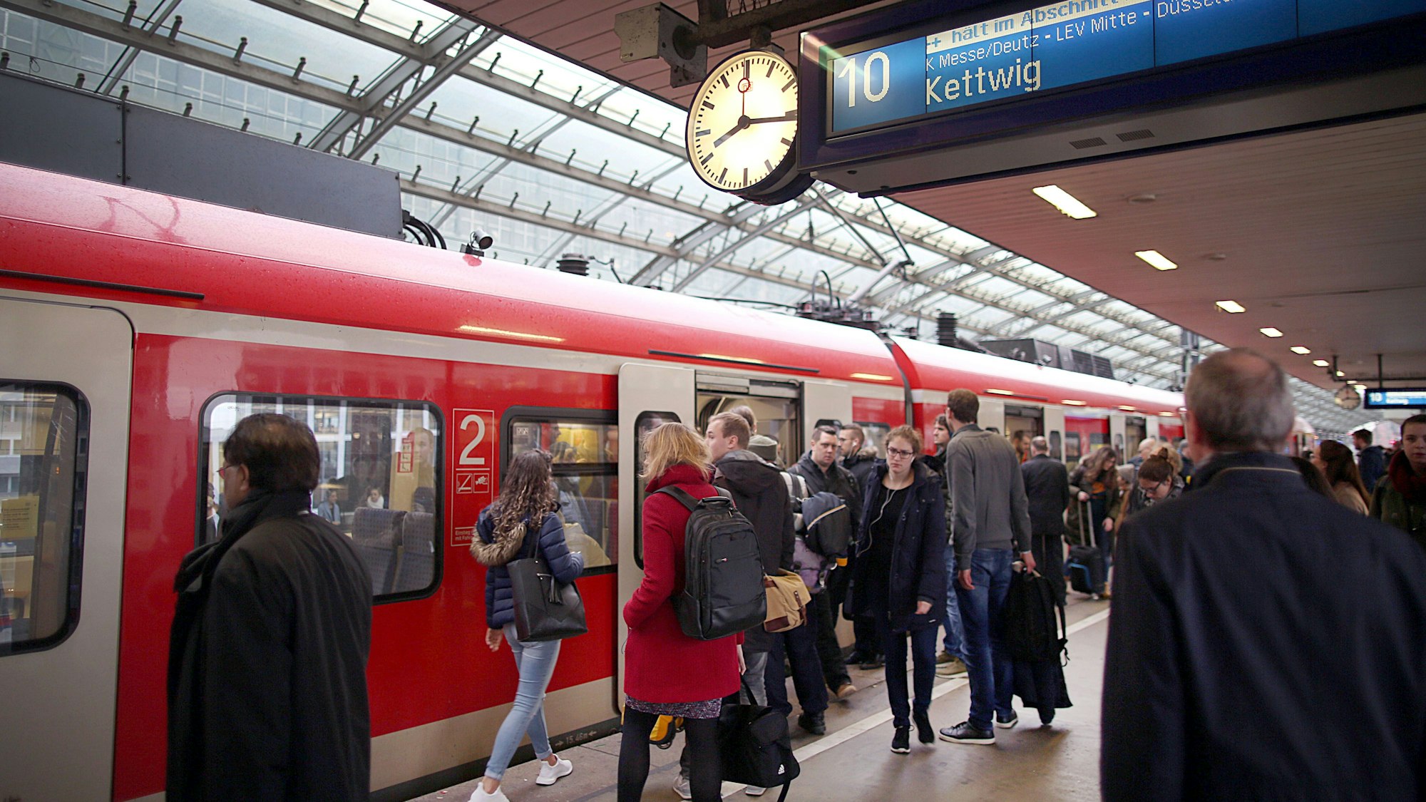Pendler stehen im Hauptbahnhof Köln vor einer S-Bahn.