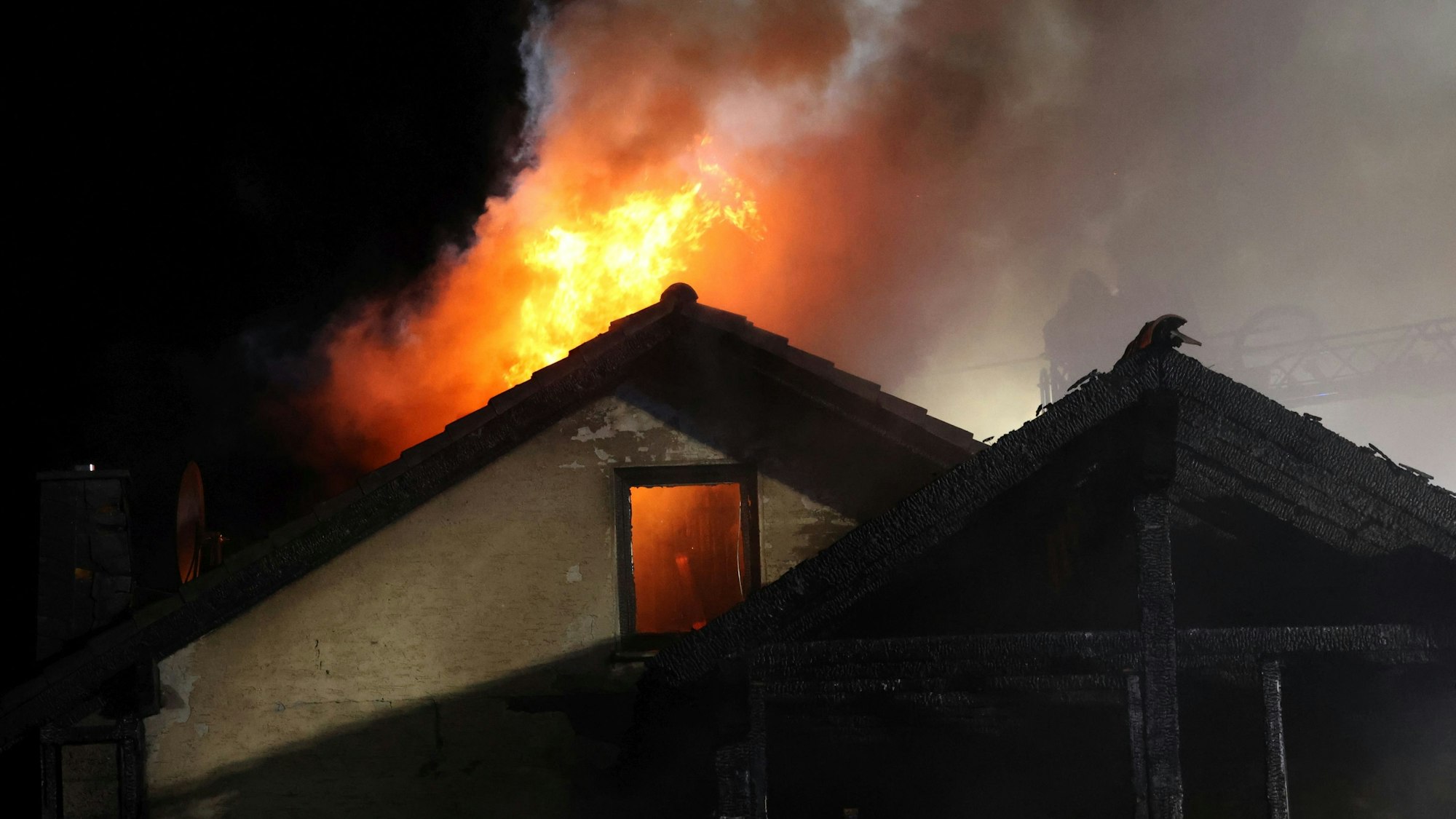 Aus einem Hausdach schlagen nachts Flammen.