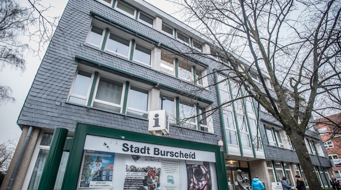 Eine grün gerahmte Info-Vitrine mit der Aufschrift „Stadt Burscheid“ vor dem verschieferten Rathaus der Stadt.