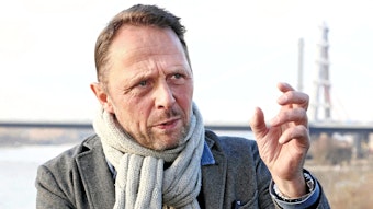 Leverkusens Oberbürgermeister Uwe Richrath, im Hintergrund sind die Rheinbrücke und der Rhein zu sehen. Richrath trägt einen Schal und gestikuliert.